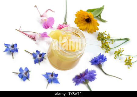 Raw organic royal jelly in a small bottle with litte spoon on small bottle surrounded by flowers on old white background. Stock Photo