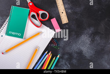 Overhead view of a notebook with pencils on a blackboard background with copy space Stock Photo