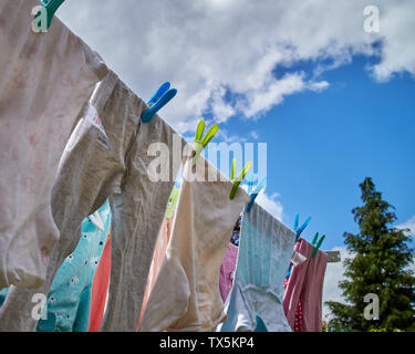 Clothes hung by pegs drying on a washing line, on a vibrant summer’s day. Stock Photo