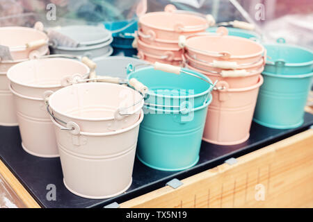 Various multicolored bright small ornamental metal buckets for sale on wooden table outdoors. Many colorful decorative mini pails for garden flower Stock Photo