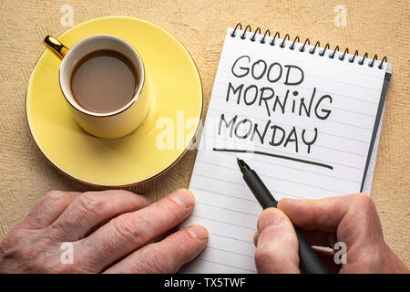 Good Morning Monday - man hand writing a note with a black marker in a spiral notebook, overhead view with a cup of coffee Stock Photo
