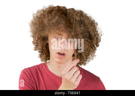 portrait of a young curly european man frightened looks at his long hair. holds a curl of hair with his fingers. very lush male guy hair. curling hair Stock Photo