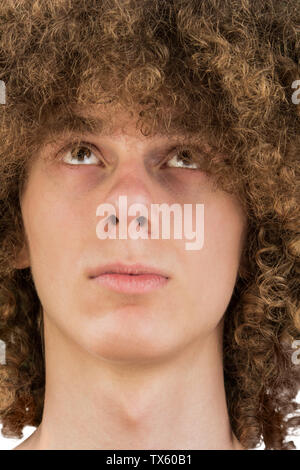 portrait of a young curly European man with a serious look looking at his long hair with his eyes up. very lush male guy hair. curling hair for men. Stock Photo