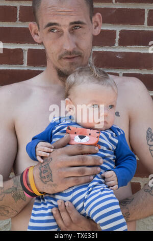 a father with tattoos holds his baby son in his arms Stock Photo