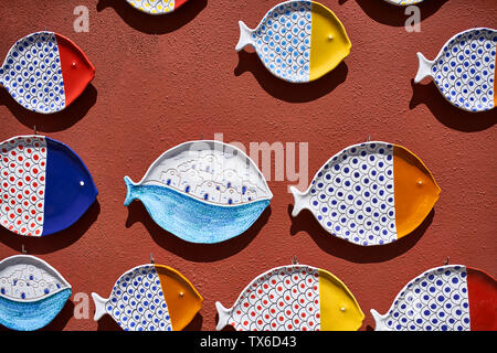 Colorful decorative ceramic plates in a form of fishes are hanging on the textured terracotta wall outdoors. They are white with red, blue, yellow, cy Stock Photo