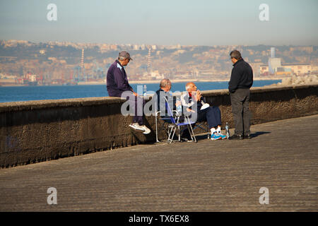 Naples, Italy - November 09, 2018: Elderly people sitting on the promenade of Naples are relaxing and talking among themselves against the background Stock Photo