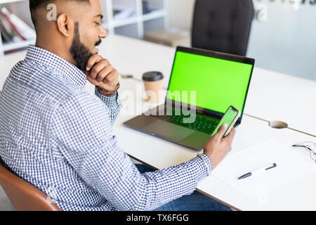 Mockup image of business man hand holding blank screen mobile smart phone while working on laptop computer in modern office, over shoulder, close up Stock Photo