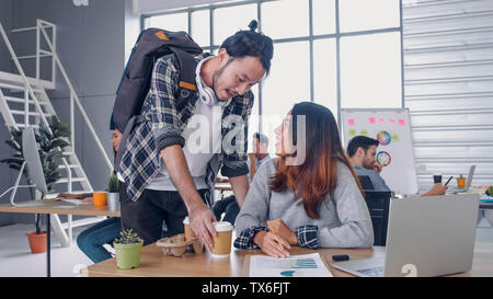 Man creative designer buy coffee cup to woman colleague at modern office in morning at desk.casual workplace lifestyle. Stock Photo