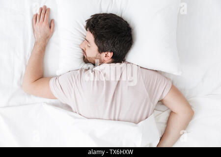 Image of a sleeping young man in the morning under blanket in bed lies. Stock Photo