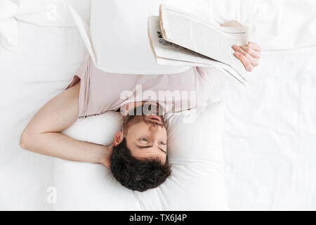 Top view of a confused handsome young man reading a newspaper while lying in bed Stock Photo