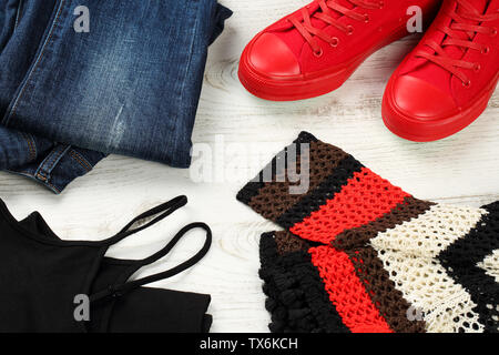 Close up, flat lay of casual clothing details for women - blue jeans, red sneakers, black sleeveless tank top and multicolored, hand knitted cotton bl Stock Photo