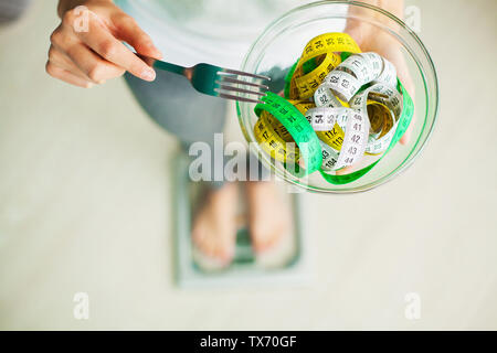Diet and Weight Loss. Woman holds bowl and fork with measuring tape Stock Photo