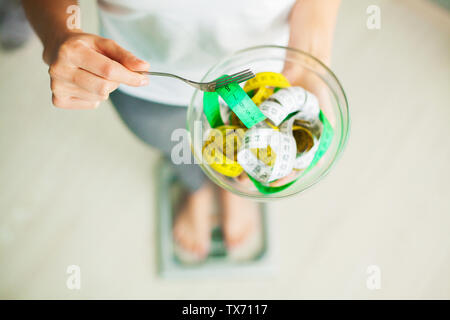 Diet and Weight Loss. Woman holds bowl and fork with measuring tape Stock Photo