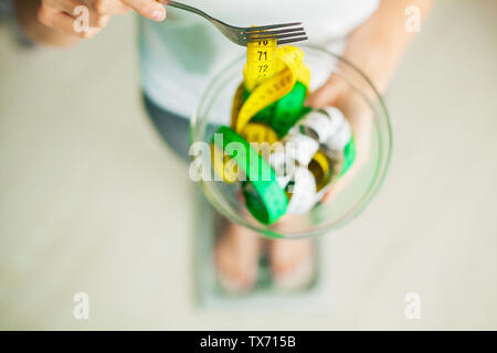 Diet and Weight Loss. Woman holds bowl and fork with measuring tape Stock Photo