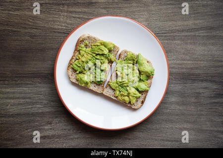 top view of two slices of homemade avocado toast on a plate on rustic wooden table - hipster food trend Stock Photo