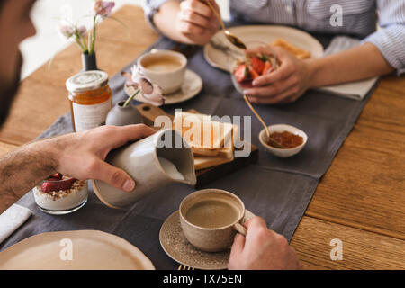 Image of modern happy couple man and woman 20s eating together at table while having breakfast in apartment Stock Photo