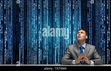 Man with folded hands looking upward. Young businessman sitting at desk. Programmer wears business suit and tie on background cyberspace with digital Stock Photo