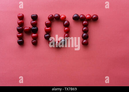 Word 'Hot' written with cherries on a pink paper background. Top view, high resolution Stock Photo