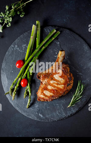 pork chop with green asparagus and cherry tomato on black background Stock Photo
