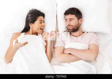 Image of a happy woman talking to her confused young man in bed under ...
