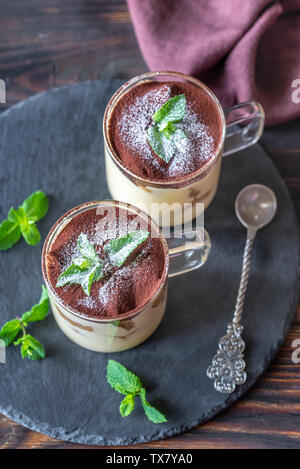 Two glass mugs of tiramisu decorated with cocoa and fresh mint leaves Stock Photo