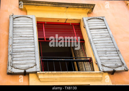Worn wooden shutters on a open window with a red blind and yellow paintwork, Italy Stock Photo