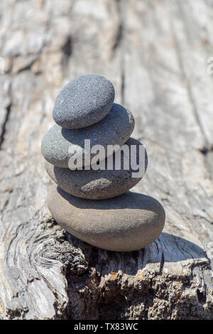 Balanced stack of four smooth stones on driftwood. Stock Photo