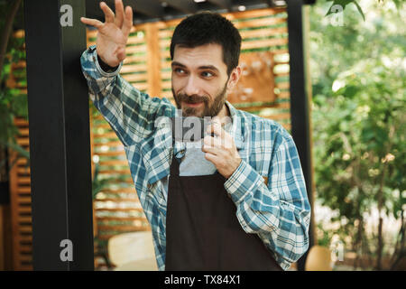 Portrait of unshaved barista man wearing apron drinking coffee while working in street cafe or coffeehouse outdoor Stock Photo