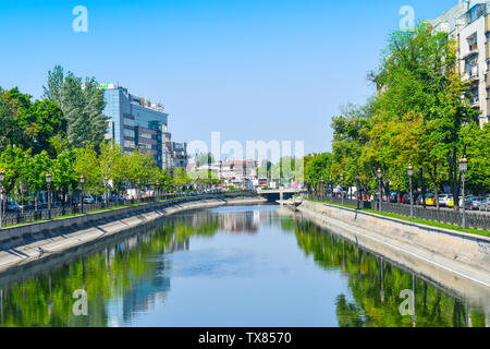 Dambovita river with buildings and trees reflected in the blue water crossing the downtown of the city Bucharest, the capital of Romania. Styled stock Stock Photo