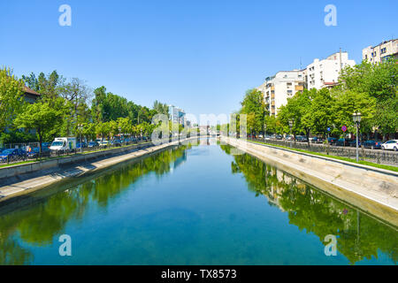 Dambovita river with buildings and trees reflected in the blue water crossing the downtown of the city Bucharest, the capital of Romania. Styled stock Stock Photo