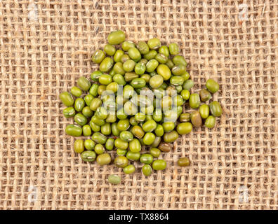 Pile of raw green mung grains scattered on burlap, top view Stock Photo