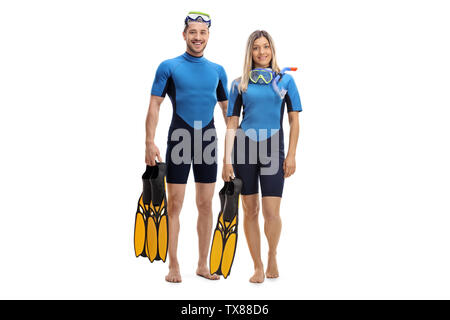 Full length portrait of a young couple in wetsuits, holding diving flippers and smiling at the camera isolated on white background Stock Photo