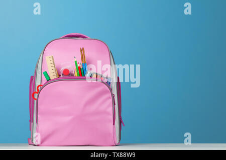 Pink backpack with office supplies on the table on a blue background. Back to school. Stock Photo