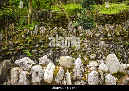 Three overlapping stone grunge walls with lichens and green vegetation in the park. Overlay stone walls texture background. Stock Photo