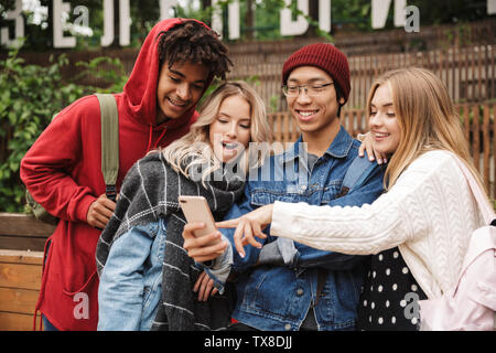 Group if cheerful multiethnic friends teenagers spending fun time together outdoors, standing, using mobile phones Stock Photo