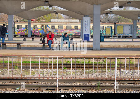 Two man sitting on bench of train platform waiting, and looking for, arrival of train in Ljubljana,  Slovenia, April 2, 2019 Stock Photo