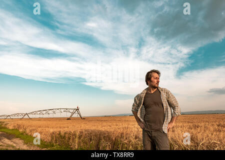 Worried farmer standing in ripe cultivated barley field while the strong wind is blowing, hoping for a better weather Stock Photo