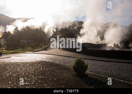 Sunny morning in a small city in a valley, with many natural hot springs, creating a steam, highlighted by the sunshine. Typical paved road and paveme Stock Photo