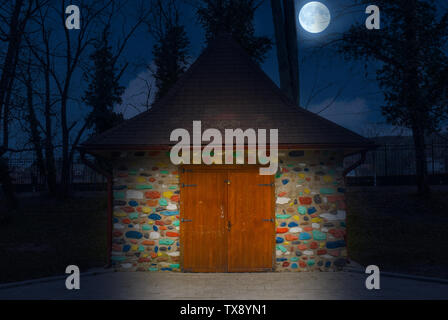 Multi-colored painted little house at night with full moon.  Colorful stone house like in fairy tales. Stock Photo
