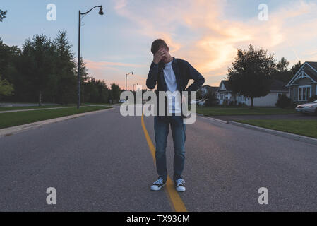 Upset teenager standing in the middle of a suburban street at sunset. Stock Photo