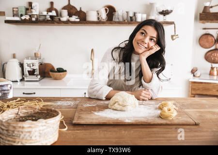 Portrait of smiling european woman 30s wearing apron cooking and making homemade pasta of dough in kitchen at home Stock Photo