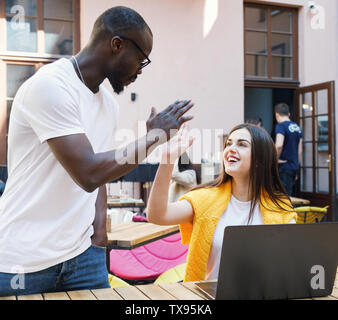 Two multicultural students giving five to each other while meeing at the cafe Stock Photo