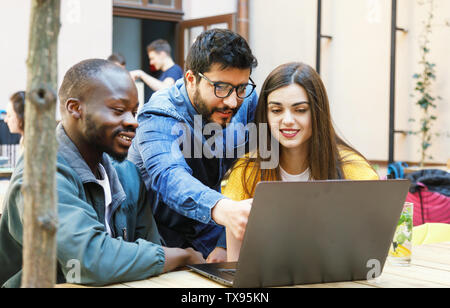 Three multicultural students discussing something at the laptop while studying at the cafe Stock Photo