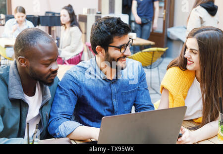 Three multicultural happy students studying together at the outdoor cafe Stock Photo