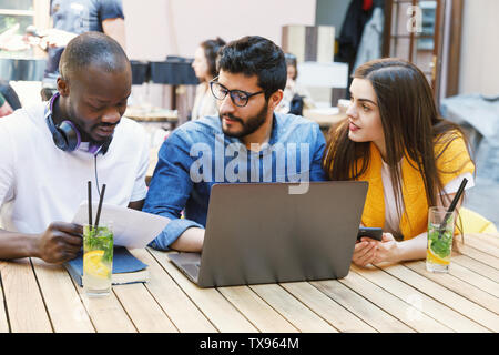 Three multicultural smart students preparing homework tasks at the outdoor cafe Stock Photo