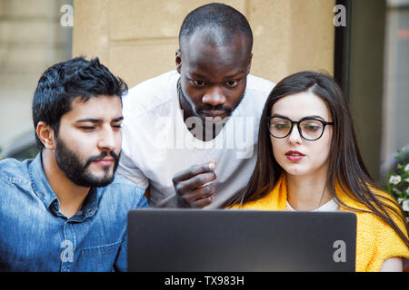 Portrait of three multicultural smart students looking at the laptop screen and discussing something Stock Photo