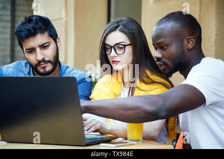 Three multicultural smart students preparing homework with laptop at the cafe Stock Photo