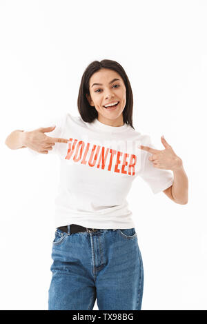 Smiling young girl wearing volunteer t-shirt standing isolated over white background, pointing Stock Photo