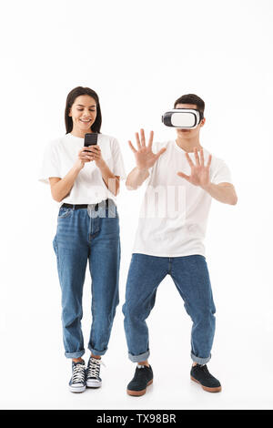 Full length portrait of a young attractive couple standing isolated over white background, wearing virtual reality headset Stock Photo