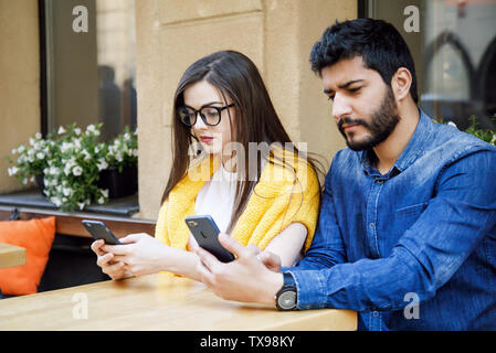 Two multicultural friends sitting at the cafe and concentrated on their smartphones Stock Photo
